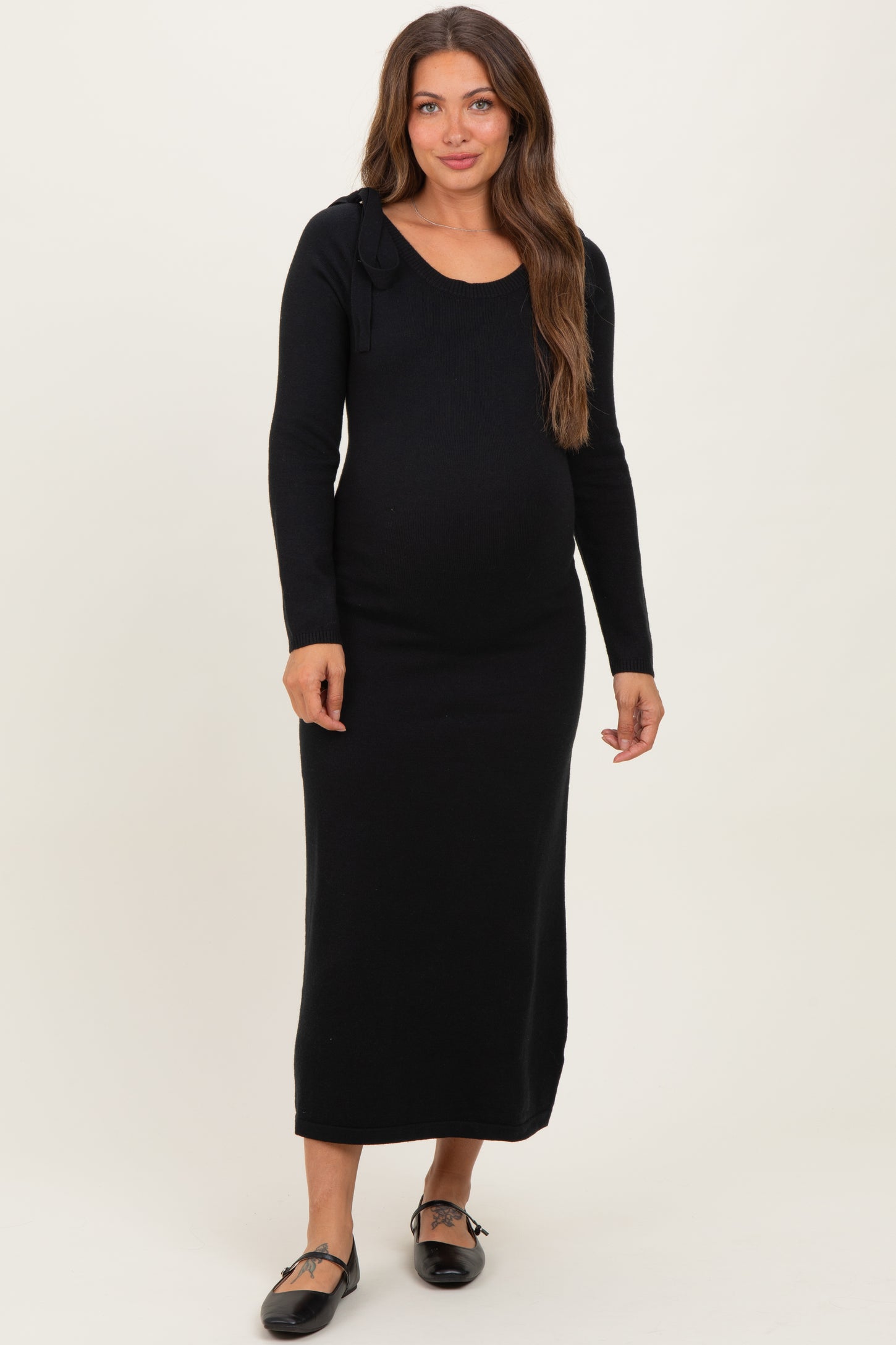 woman wearing a black long sleeve maternity dress with a scoop neckline and side tie detail, showcasing her baby bump