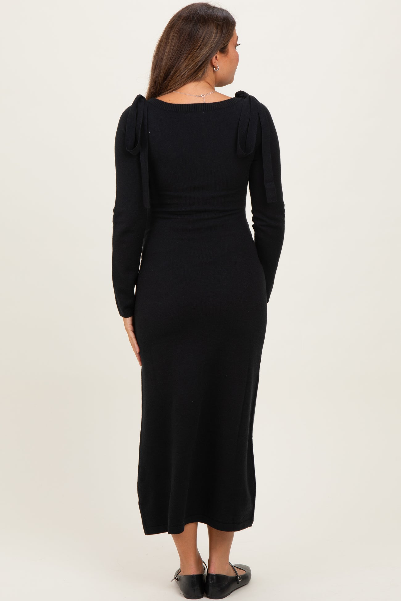 woman wearing a black long sleeve maternity dress with tie details on the shoulders
