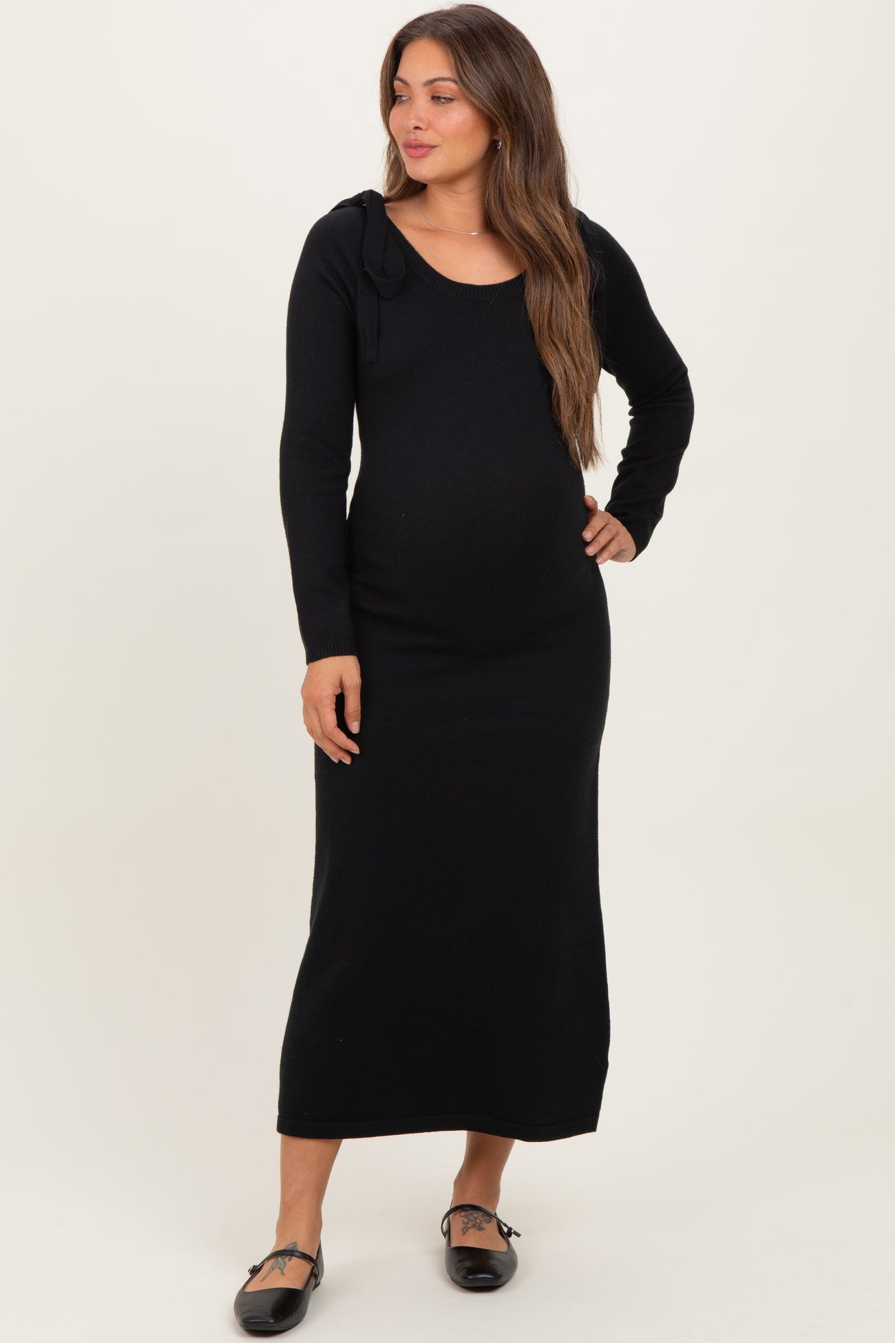 woman wearing a black long sleeve maternity dress with a fitted silhouette and shoulder tie details, showing a baby bump