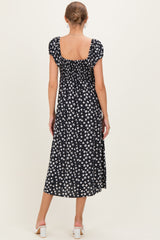 woman wearing a black floral maternity dress with a square neckline and short puff sleeves, showing a flowing hemline