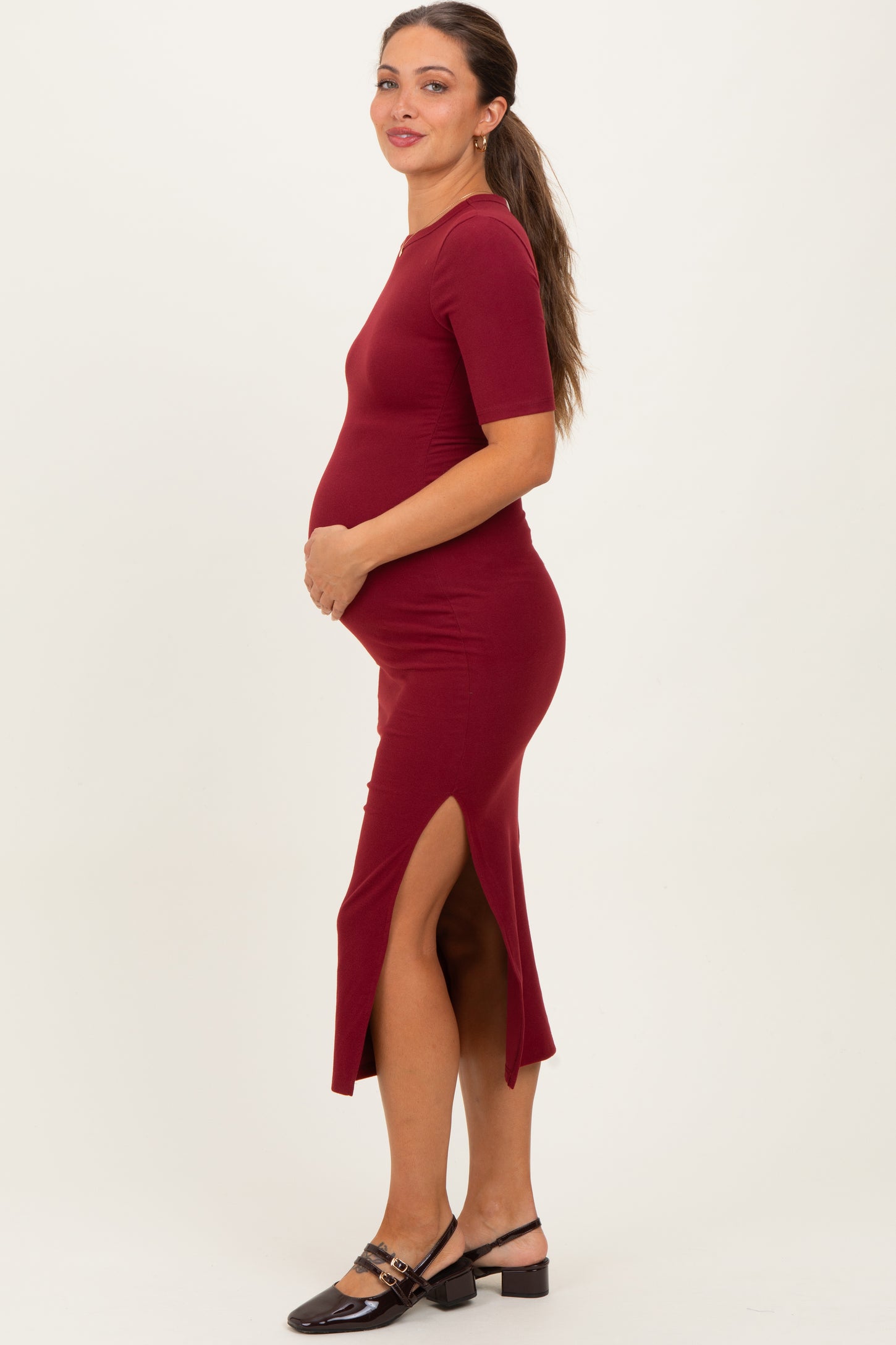 woman wearing a burgundy maternity dress with short sleeves and side slits, showcasing her baby bump