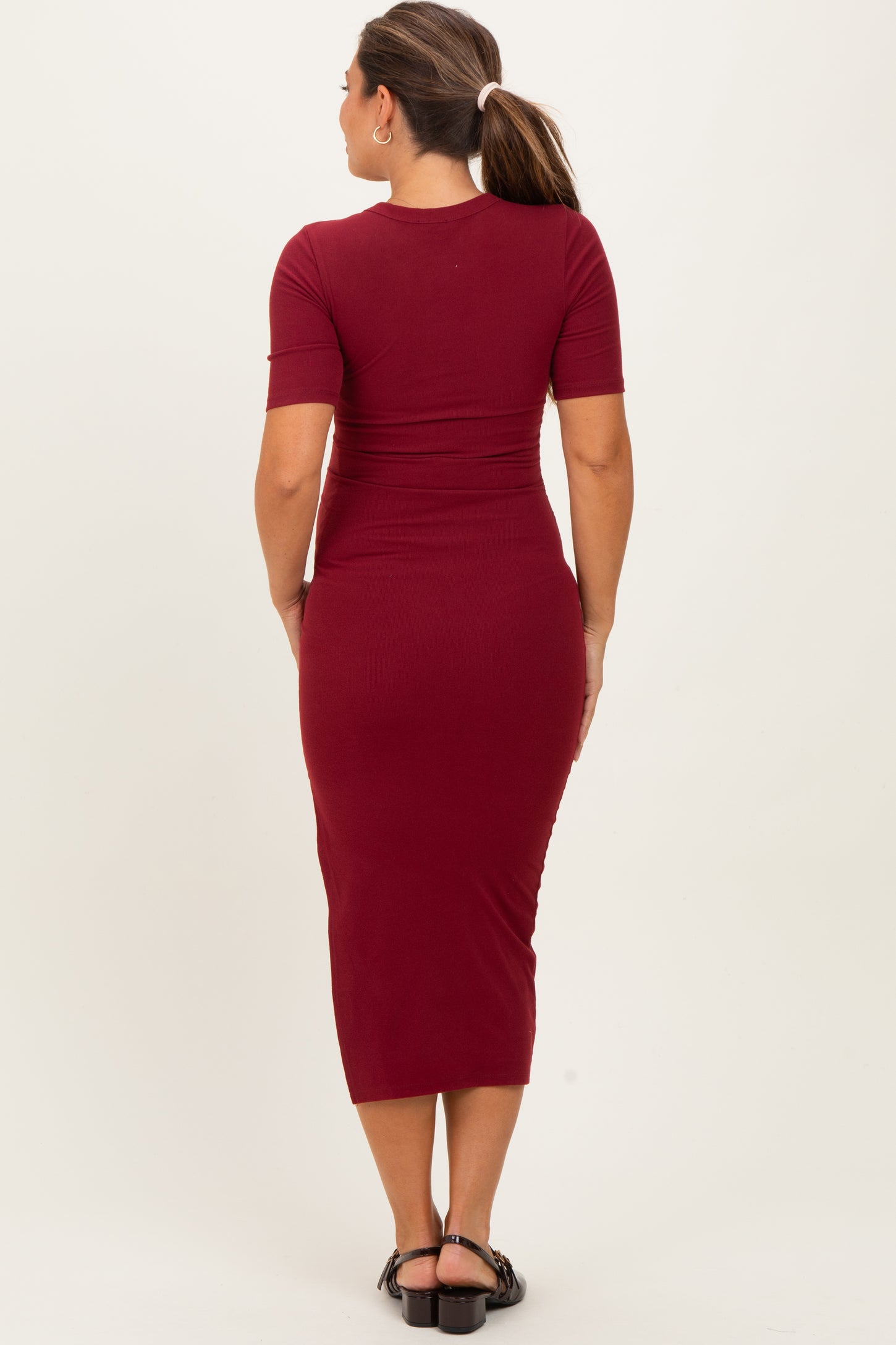 woman wearing a burgundy short sleeve maternity dress with a form-fitting silhouette and midi length