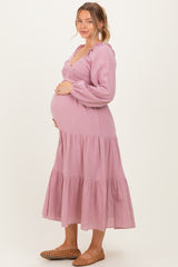 woman wearing a light pink maternity dress with long sleeves and a tiered skirt, showcasing her baby bump