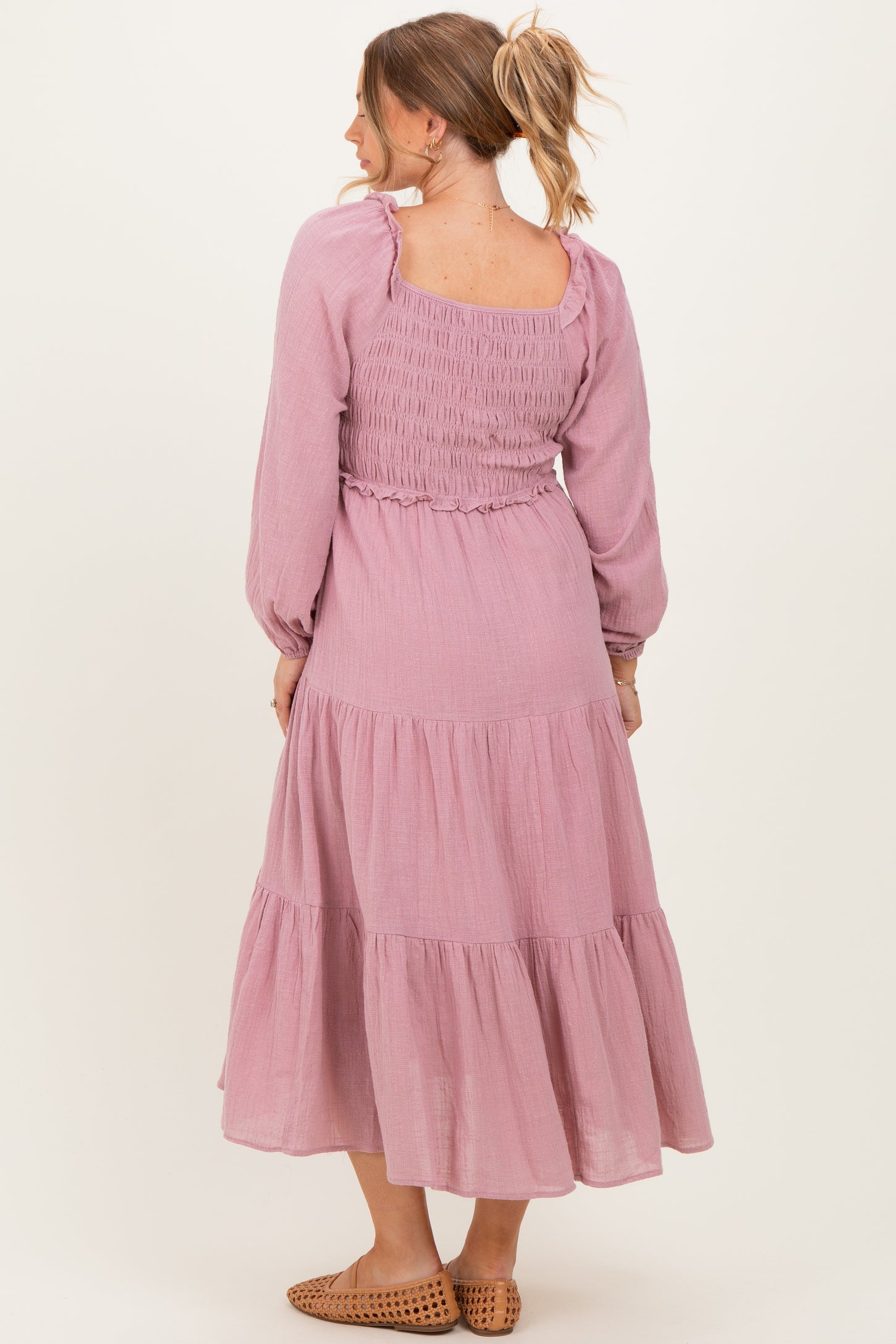 woman wearing a mauve long sleeve maternity dress with smocked bodice and tiered skirt, showing baby bump