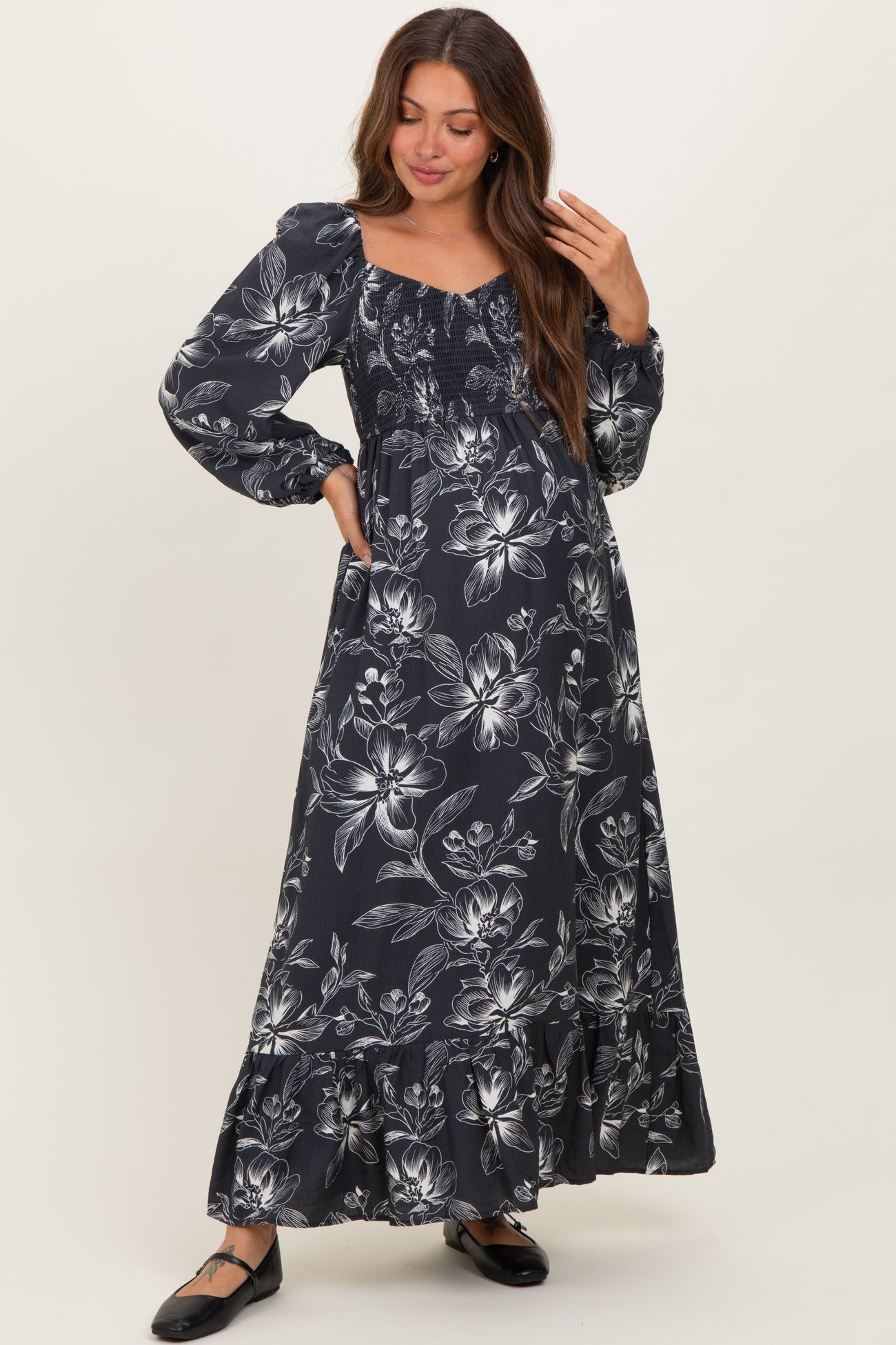 woman wearing a dark floral maternity maxi dress with puffed sleeves and a smocked bodice, showcasing her baby bump