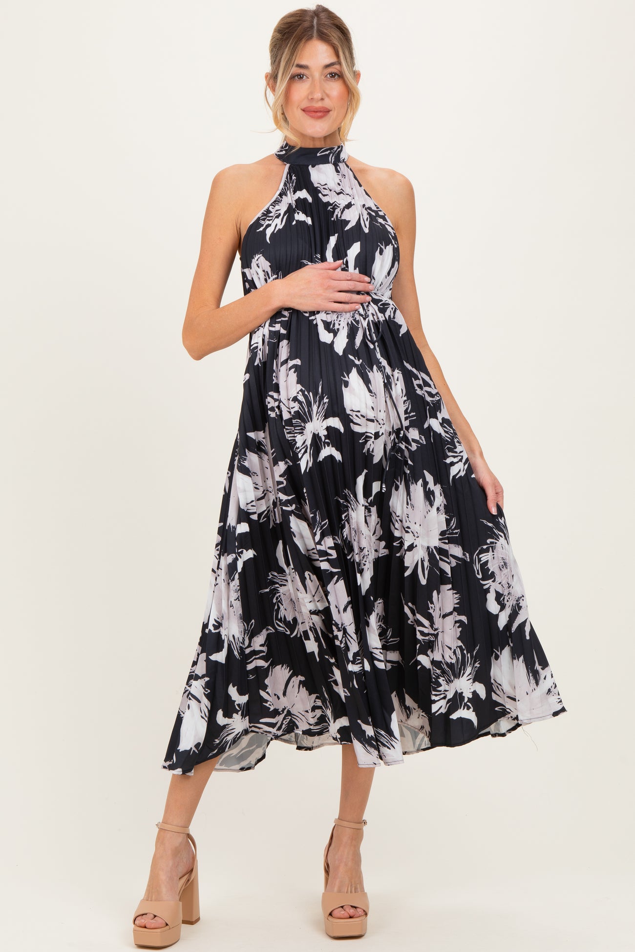 woman wearing a black and white floral print maternity dress with a halter neck and flowing skirt, standing with one hand on her baby bump