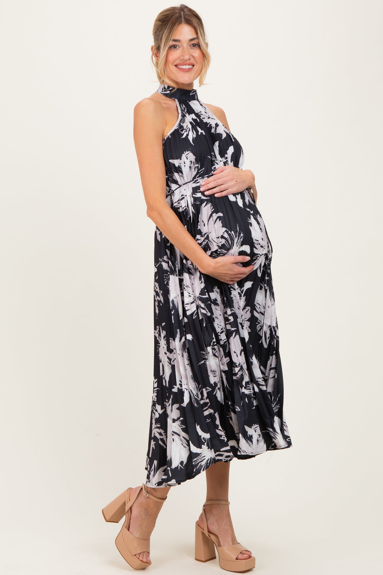 woman wearing a black and white floral maternity dress, cradling her baby bump