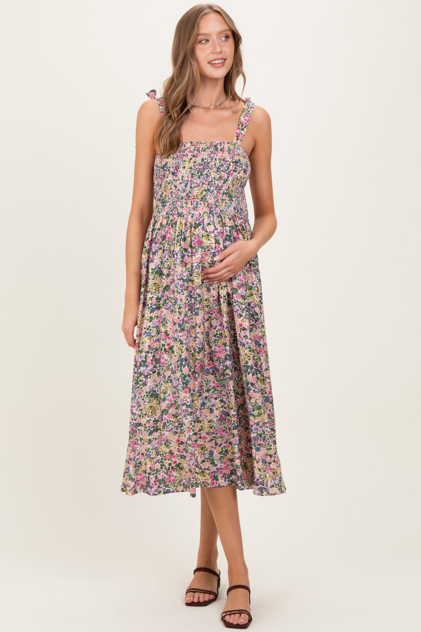 woman wearing a floral maternity dress with smocked bodice and adjustable straps, holding her baby bump