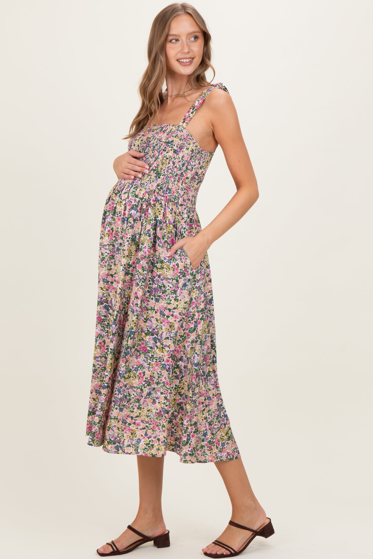 woman wearing a floral print maternity dress with a smocked bodice and adjustable straps, holding her baby bump
