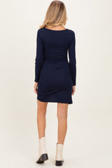 woman wearing a navy blue long sleeve maternity dress with ruched detailing and a fitted silhouette