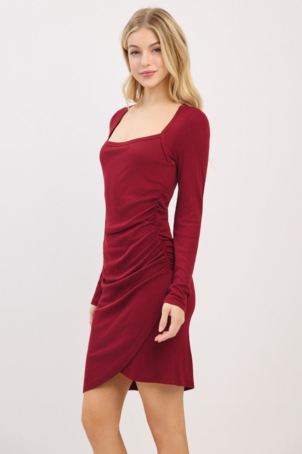woman wearing a burgundy long sleeve mini dress with a square neckline and side ruching detail