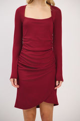 woman wearing a burgundy long sleeve fitted dress with a square neckline and side ruching details