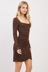woman wearing a brown ribbed long sleeve mini dress with ruched detailing and a scoop neckline