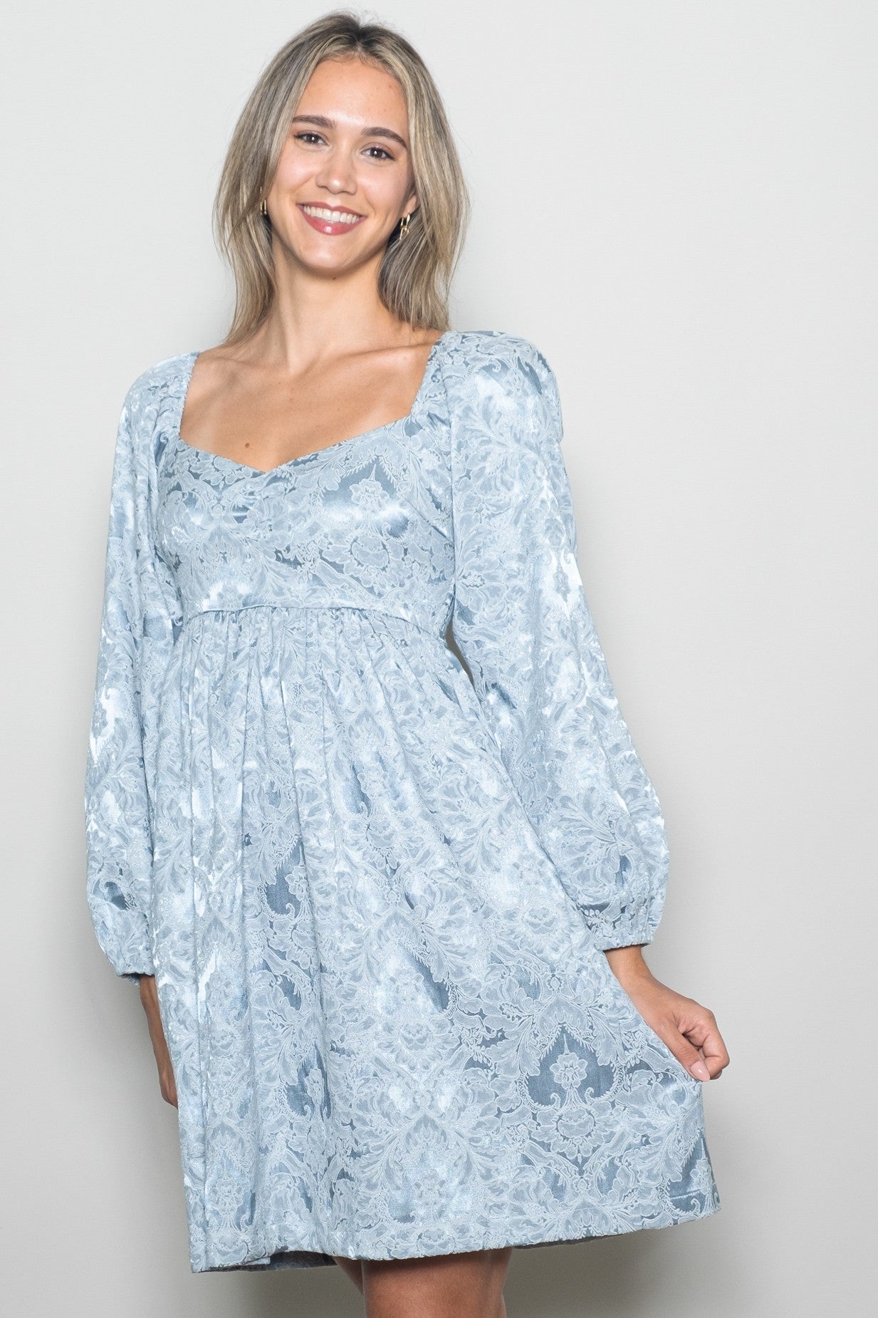 woman wearing a light blue lace dress with a square neckline and puff sleeves, smiling at the camera