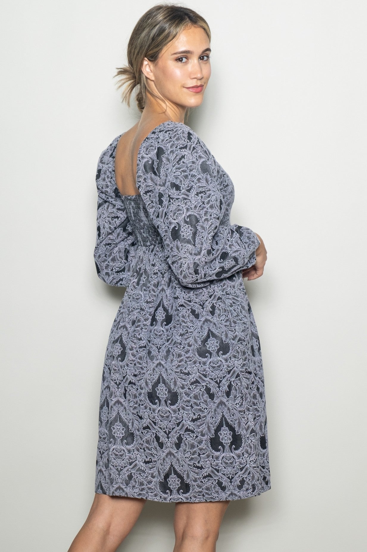 woman wearing a gray patterned long sleeve dress with a fitted waist and open back