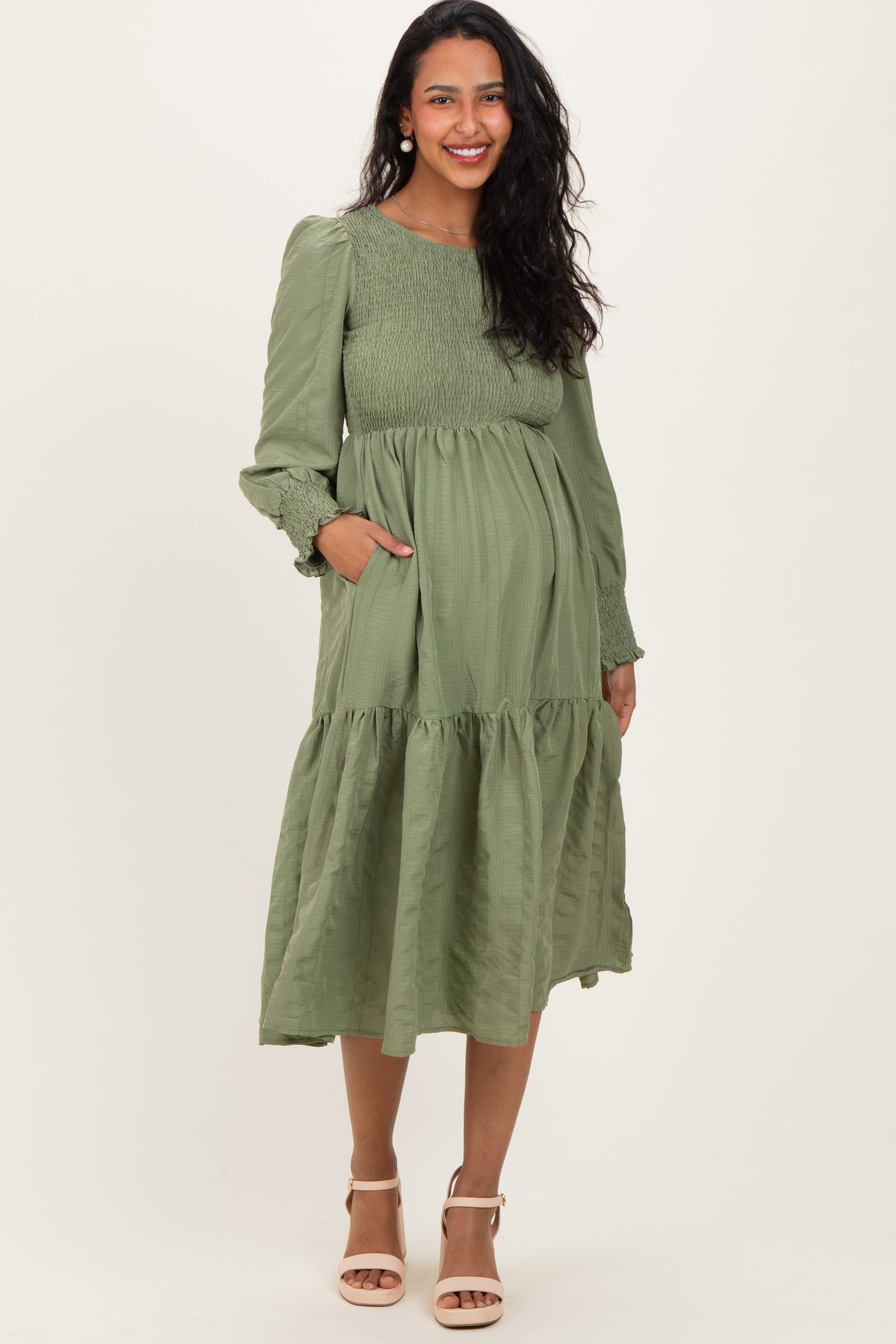 woman wearing a dark green long sleeve maternity dress with a flared skirt and pockets, showing her baby bump