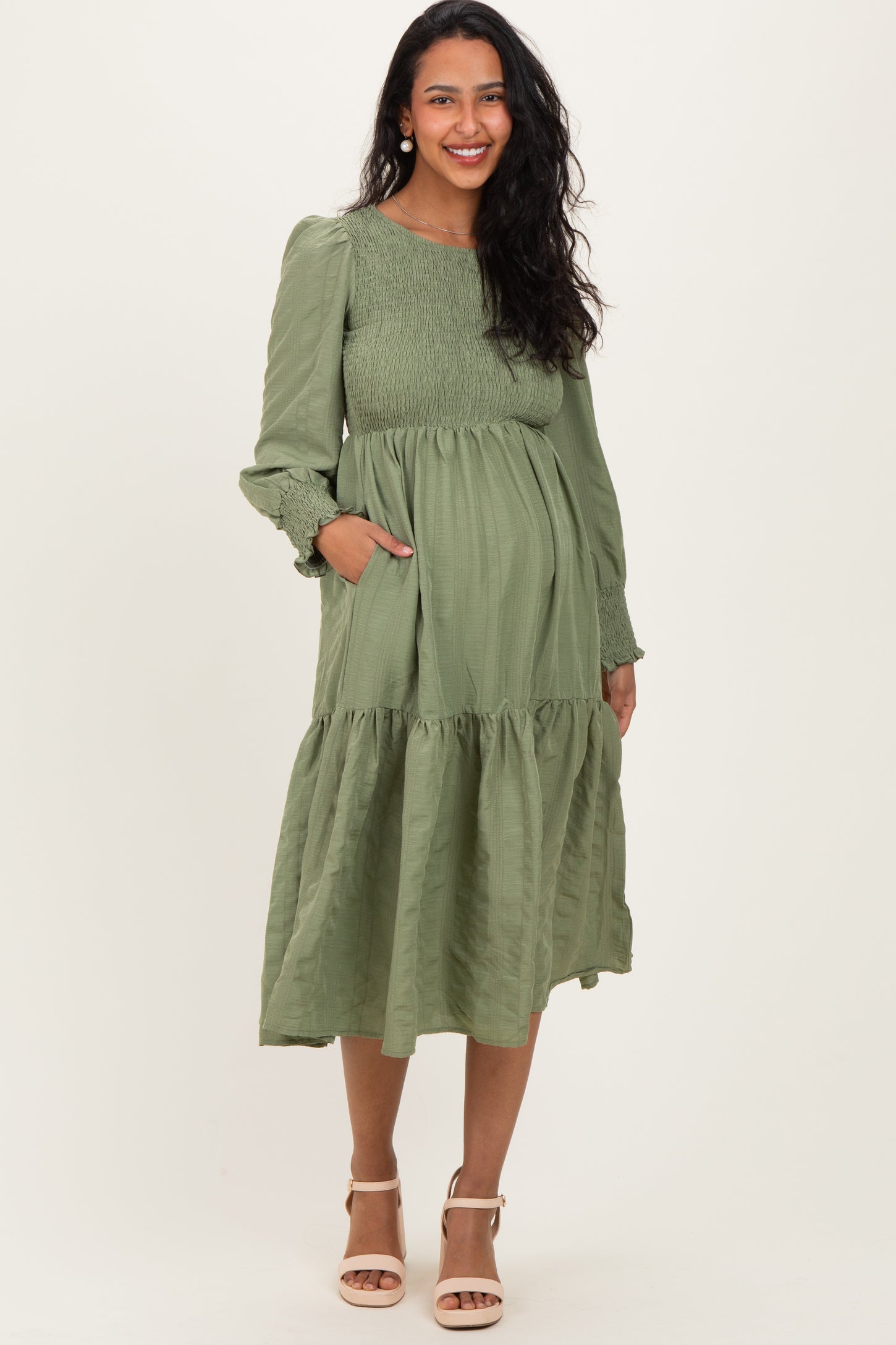 woman wearing a dark green long sleeve maternity dress with a flared skirt and pockets, showing her baby bump