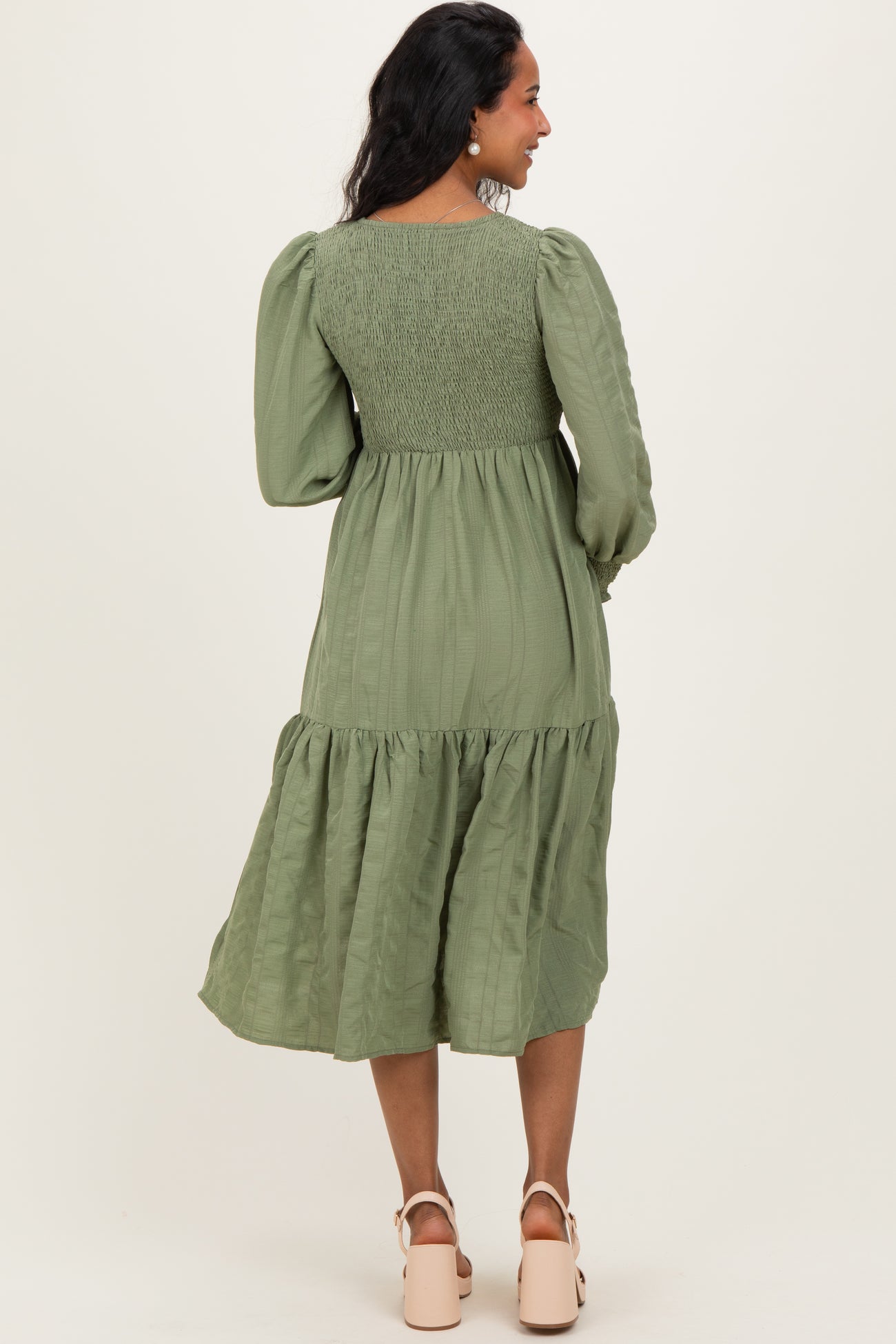 woman wearing an olive green maternity dress with puff sleeves and a tiered skirt, showing a baby bump from the back