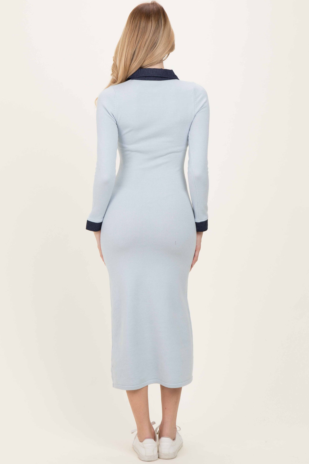 woman wearing a light blue ribbed long sleeve dress with a navy collar and mid-calf length, facing away from the camera