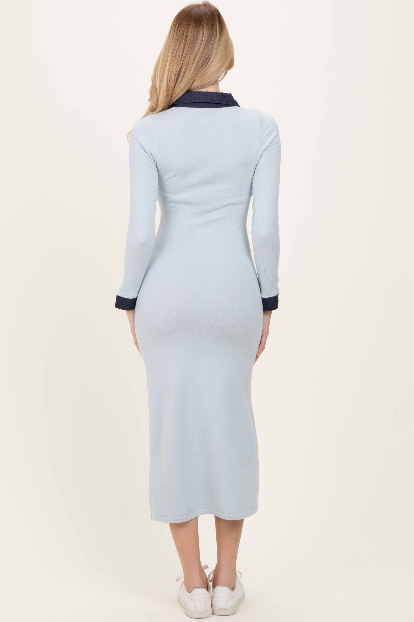 woman wearing a light blue ribbed long sleeve dress with a navy collar and mid-calf length, facing away from the camera