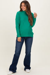 woman wearing a green long sleeve maternity sweater and flared jeans, with a visible baby bump