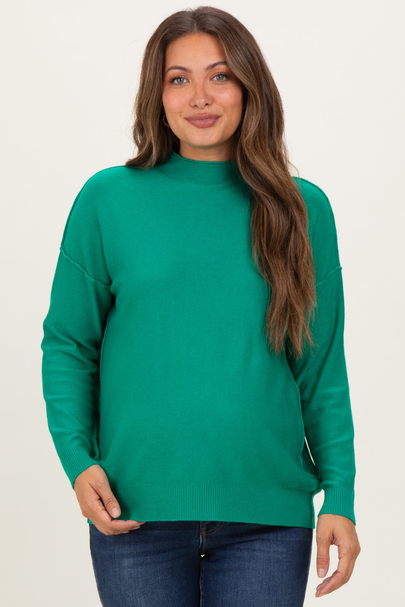 woman wearing a green long sleeve maternity sweater with a high neck and relaxed fit, showing her baby bump