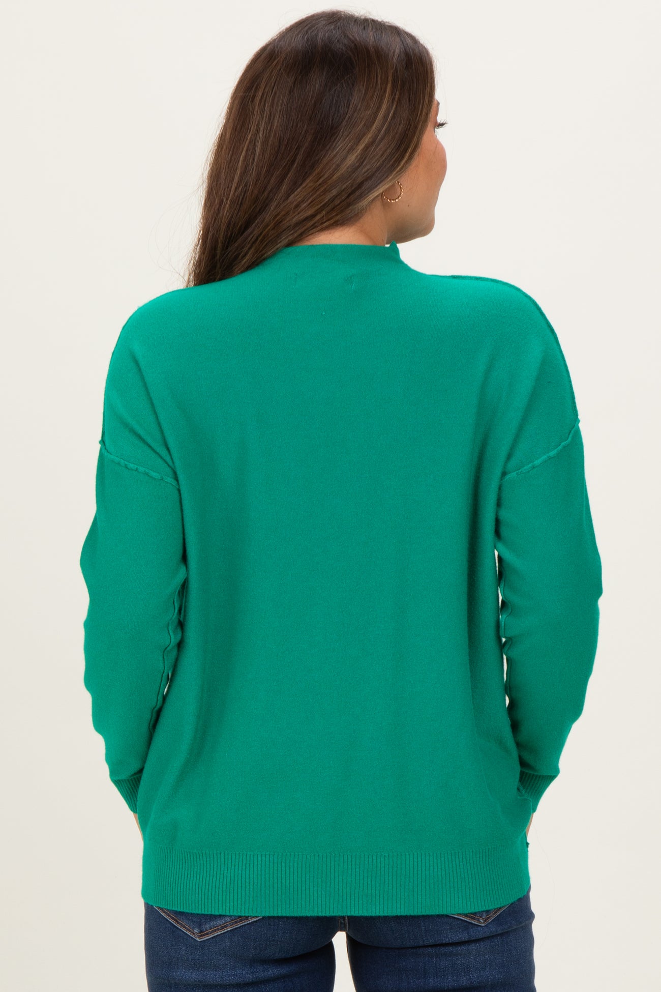 woman wearing a green maternity sweater, showing a relaxed fit and back details, with blue jeans