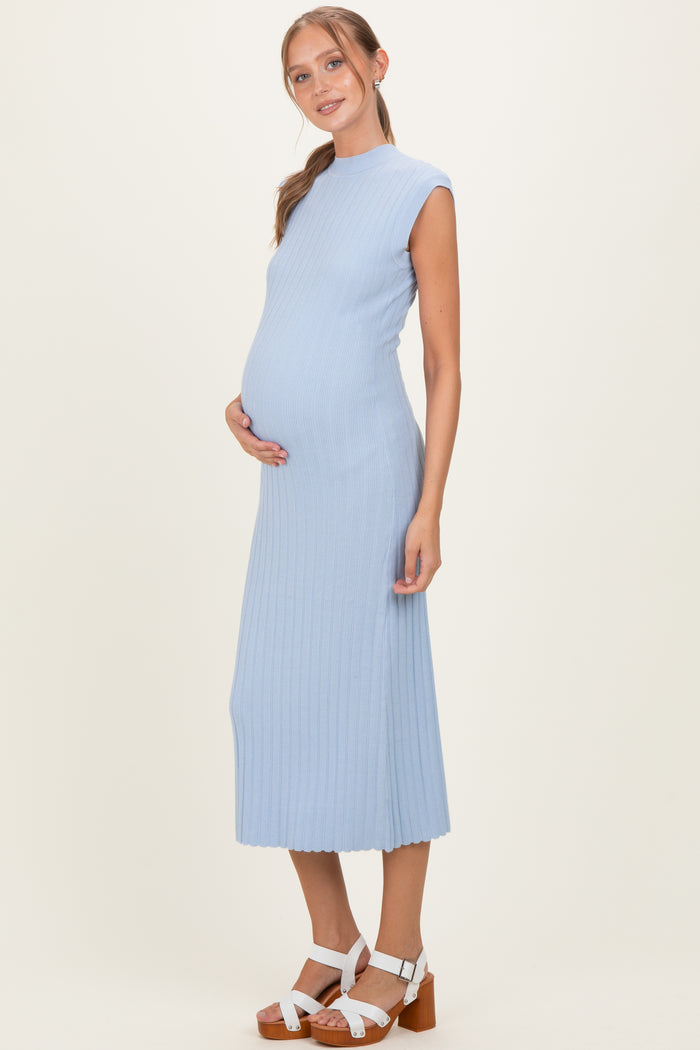 woman wearing a light blue ribbed maternity dress, showcasing her baby bump while standing with a neutral background