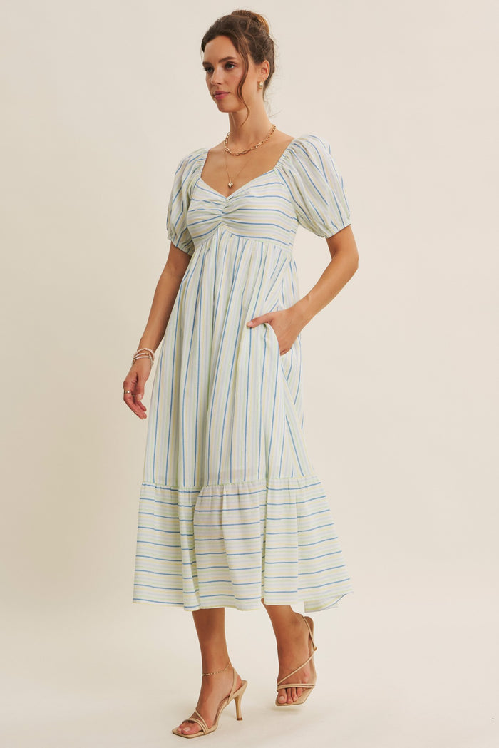 woman wearing a striped midi dress with puff sleeves and pockets, styled with strappy heels