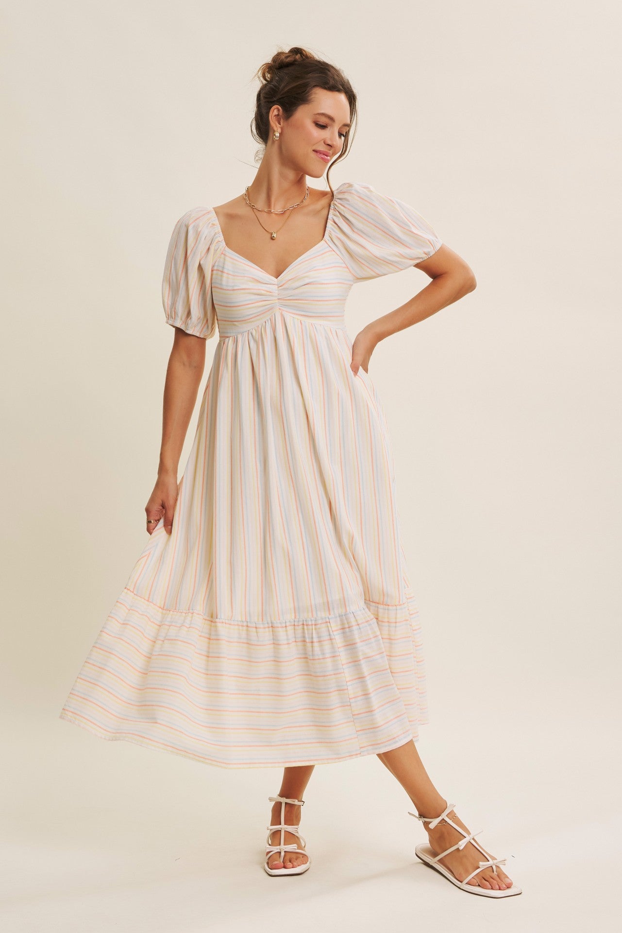 woman wearing a striped maxi dress with puff sleeves and a tiered bottom, posing against a neutral background