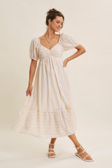 woman wearing a striped maxi dress with puff sleeves and a tiered bottom, posing against a neutral background