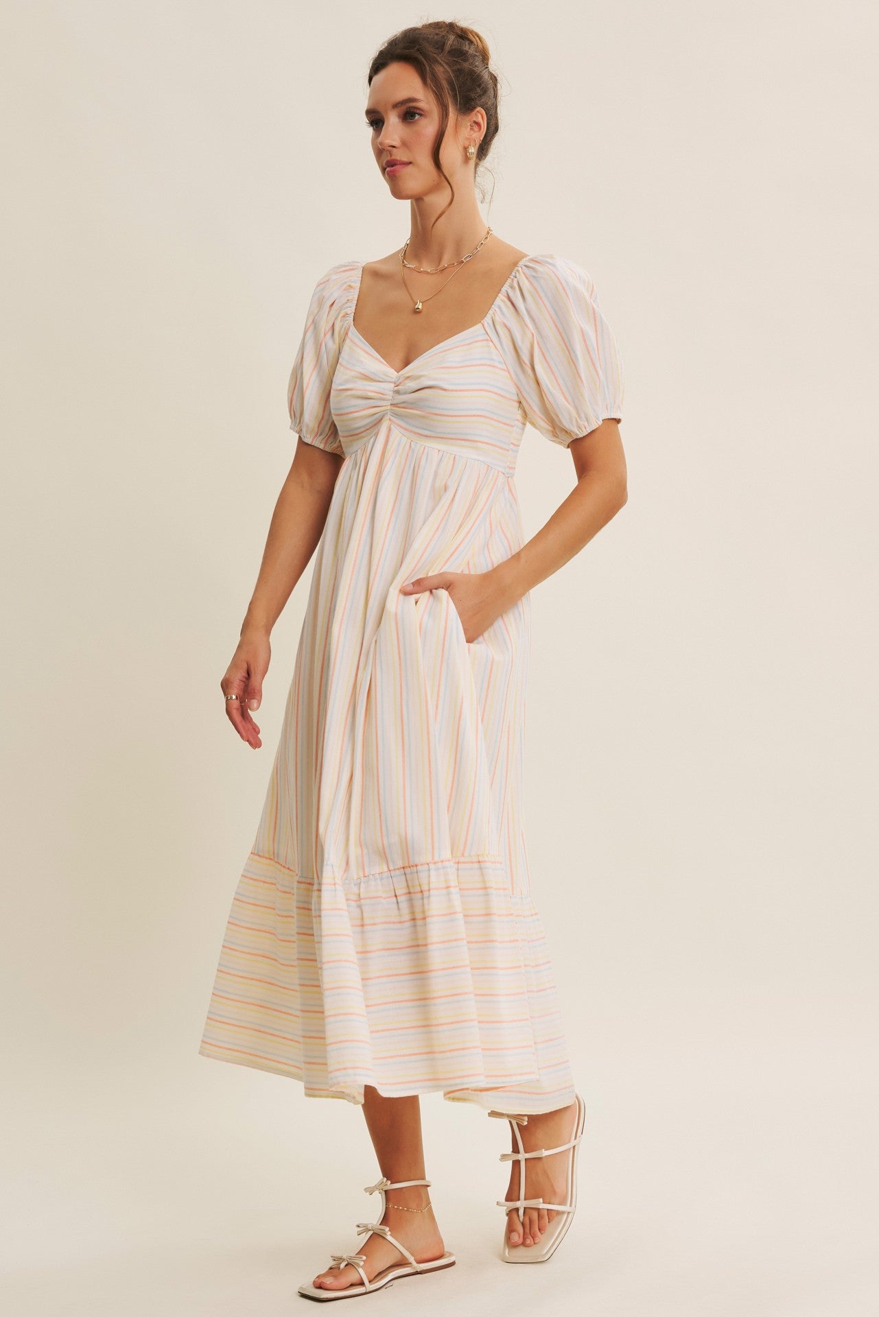 woman wearing a striped midi dress with puff sleeves and a sweetheart neckline, featuring side pockets and a tiered hemline