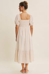 woman wearing a cream and striped mid-length summer dress with puff sleeves and a smocked bodice seen from the back