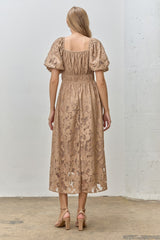 woman wearing a beige puff sleeve midi dress with a fitted waist and floral lace detailing, shown from the back