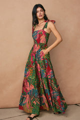 woman wearing a colorful floral maxi dress with tie straps and pockets, standing against a textured background