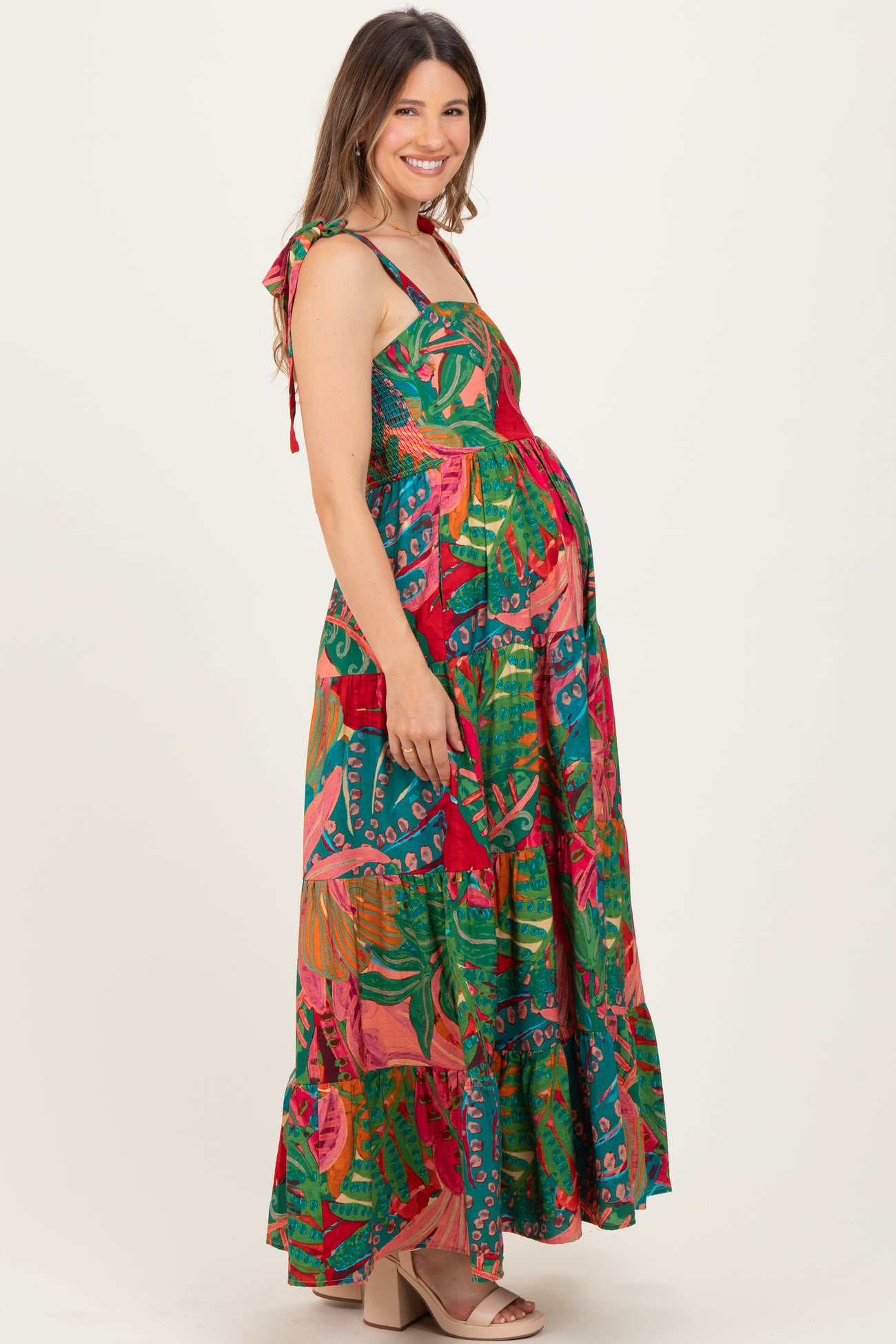 woman wearing a colorful floral maternity maxi dress with tie shoulder straps and a visible baby bump