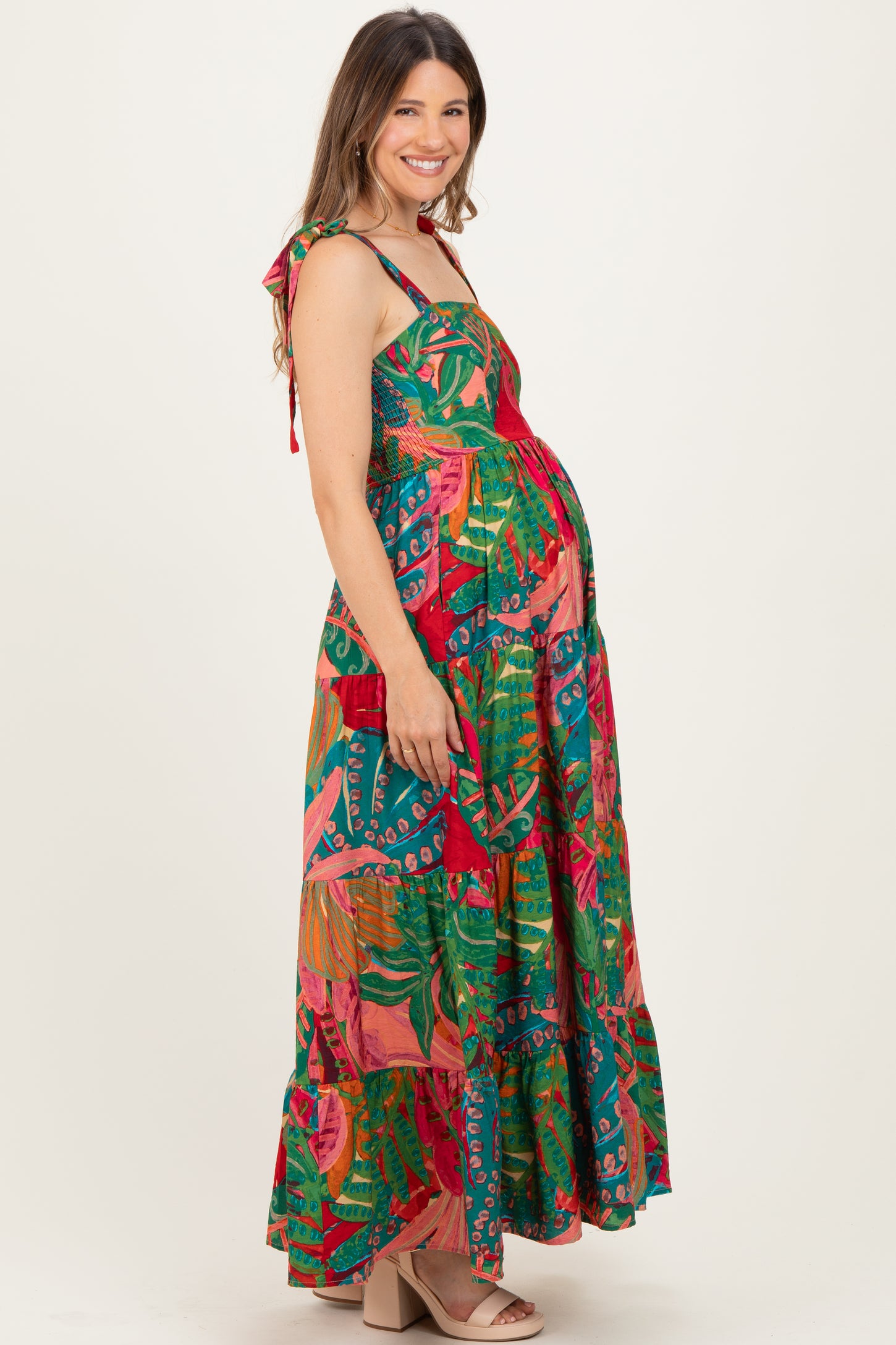woman wearing a colorful floral maternity maxi dress with tie shoulder straps and a visible baby bump
