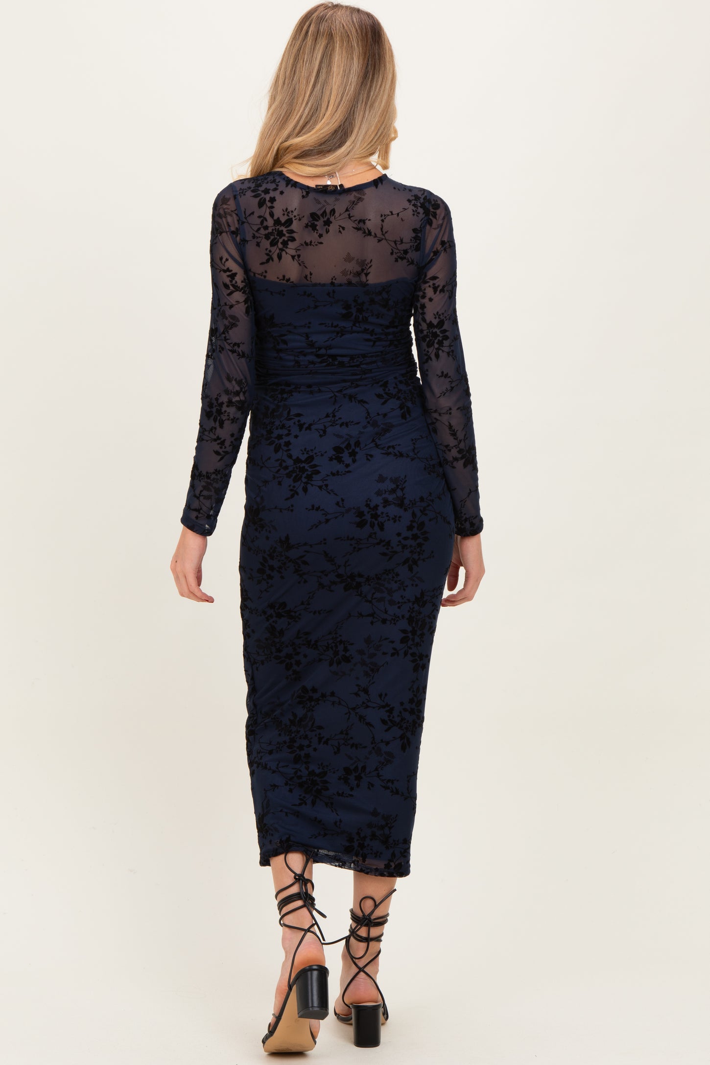 woman wearing a navy blue long sleeve maternity dress with floral lace details and a fitted silhouette.