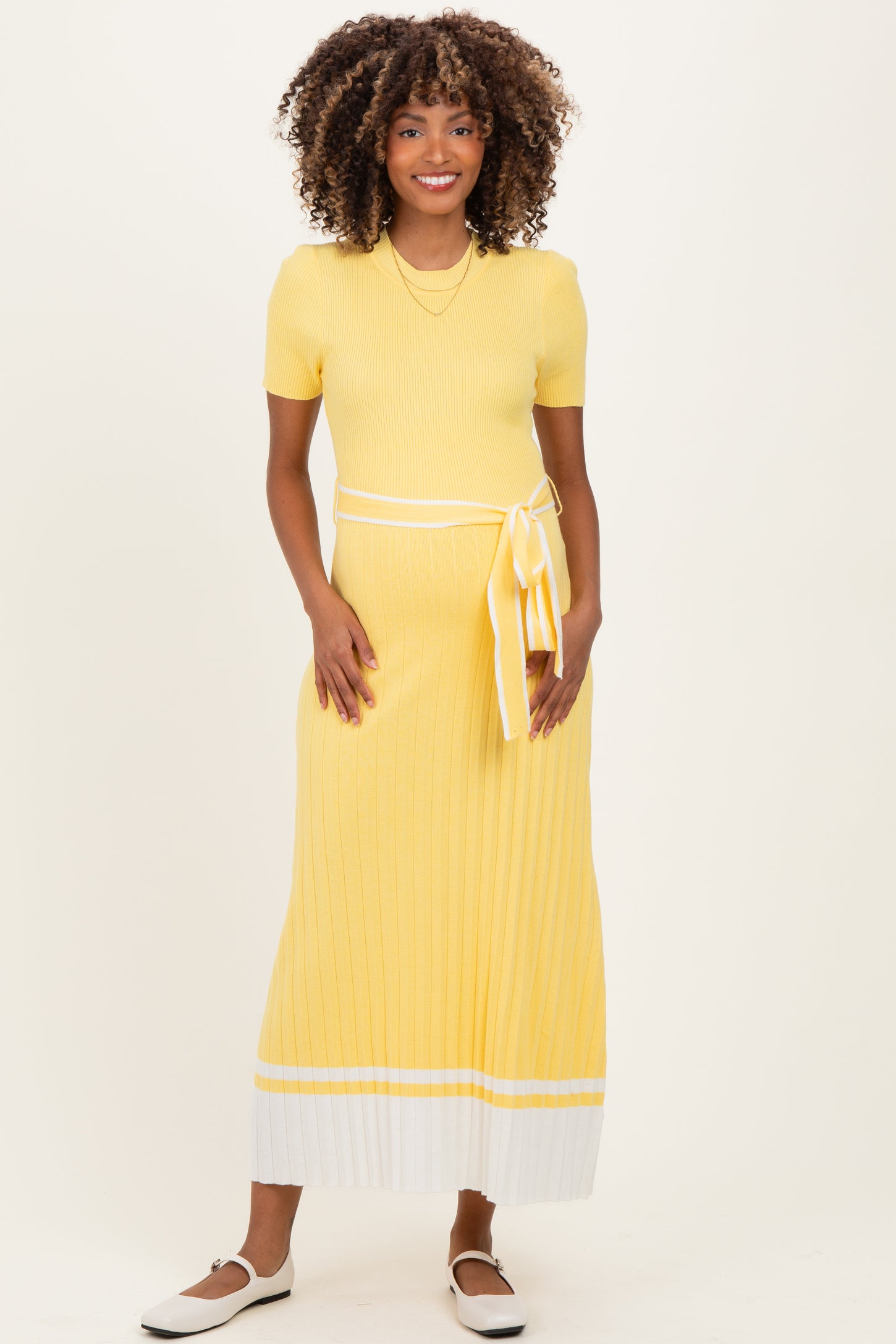 woman wearing a yellow ribbed maternity dress with a tie waist and white striped detailing at the hem