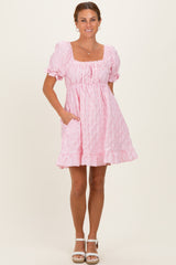 woman wearing a pink short puff sleeve dress with a square neckline and a ruffled hem, standing with hands in pockets