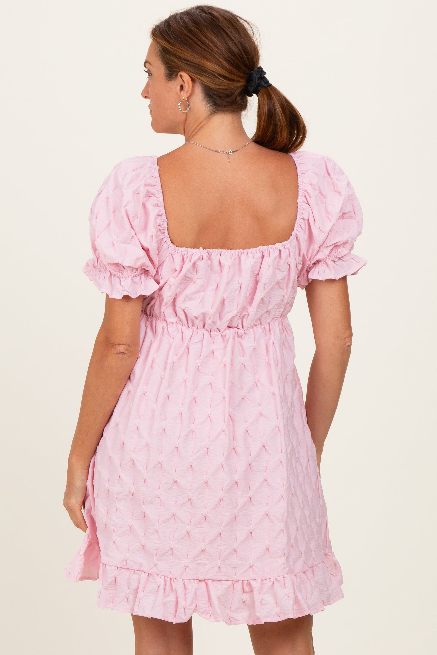 woman wearing a pink puff sleeve dress with a square neckline and ruffled hem, shown from the back