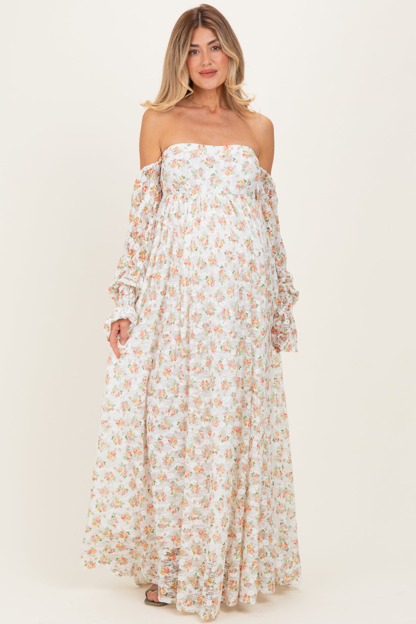 woman wearing a floral off-the-shoulder maternity dress with long sleeves and a flowing silhouette, showing a baby bump