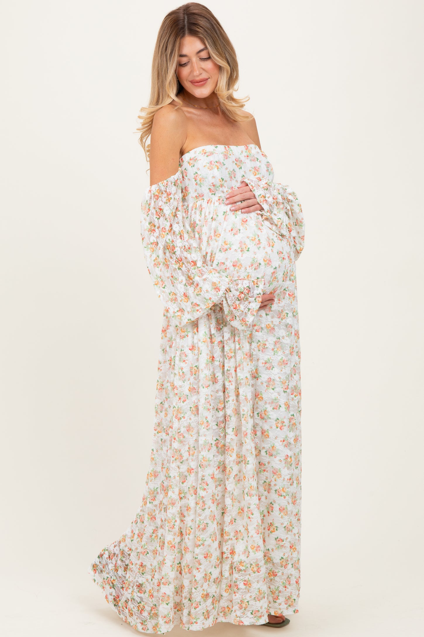 woman wearing a strapless floral maternity gown with puff sleeves, holding her baby bump