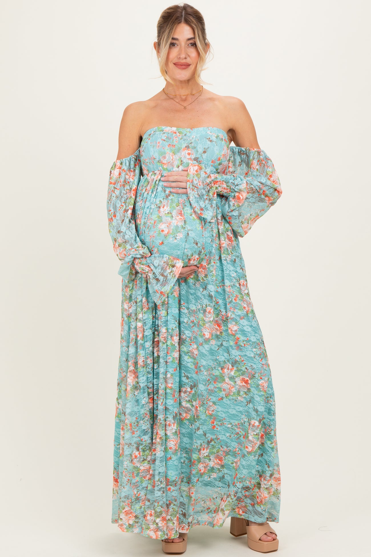 woman wearing a floral off-shoulder maternity maxi dress and holding her baby bump