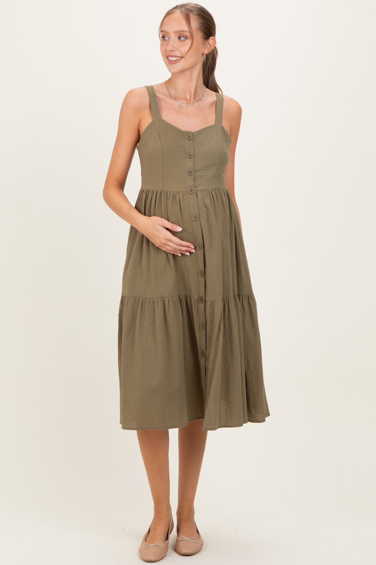 woman wearing an olive green maternity dress with button details and a tiered skirt, holding her baby bump