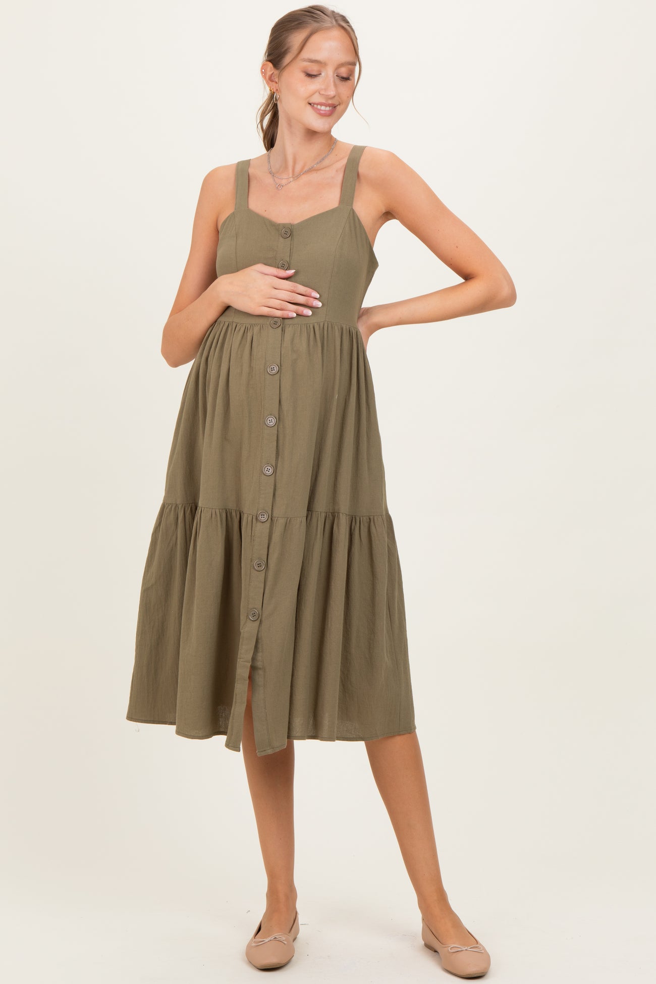 woman wearing an olive green maternity button-up dress with a tiered skirt and holding her baby bump