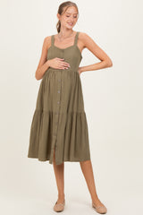 woman wearing an olive green maternity button-up dress with a tiered skirt and holding her baby bump