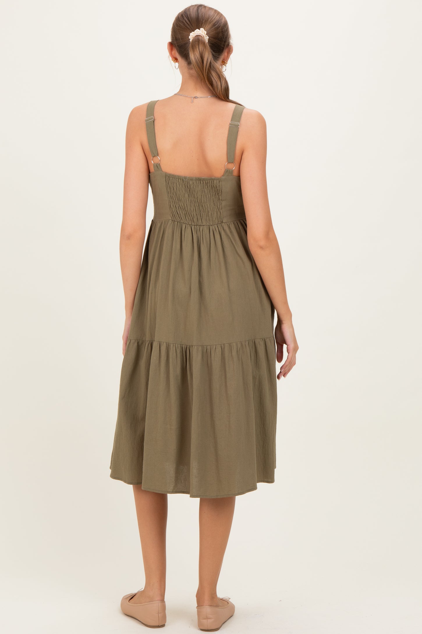 woman wearing a sage green maternity dress with adjustable straps and a tiered skirt, showing the back view