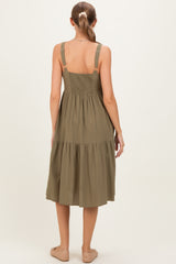 woman wearing a sage green maternity dress with adjustable straps and a tiered skirt, showing the back view