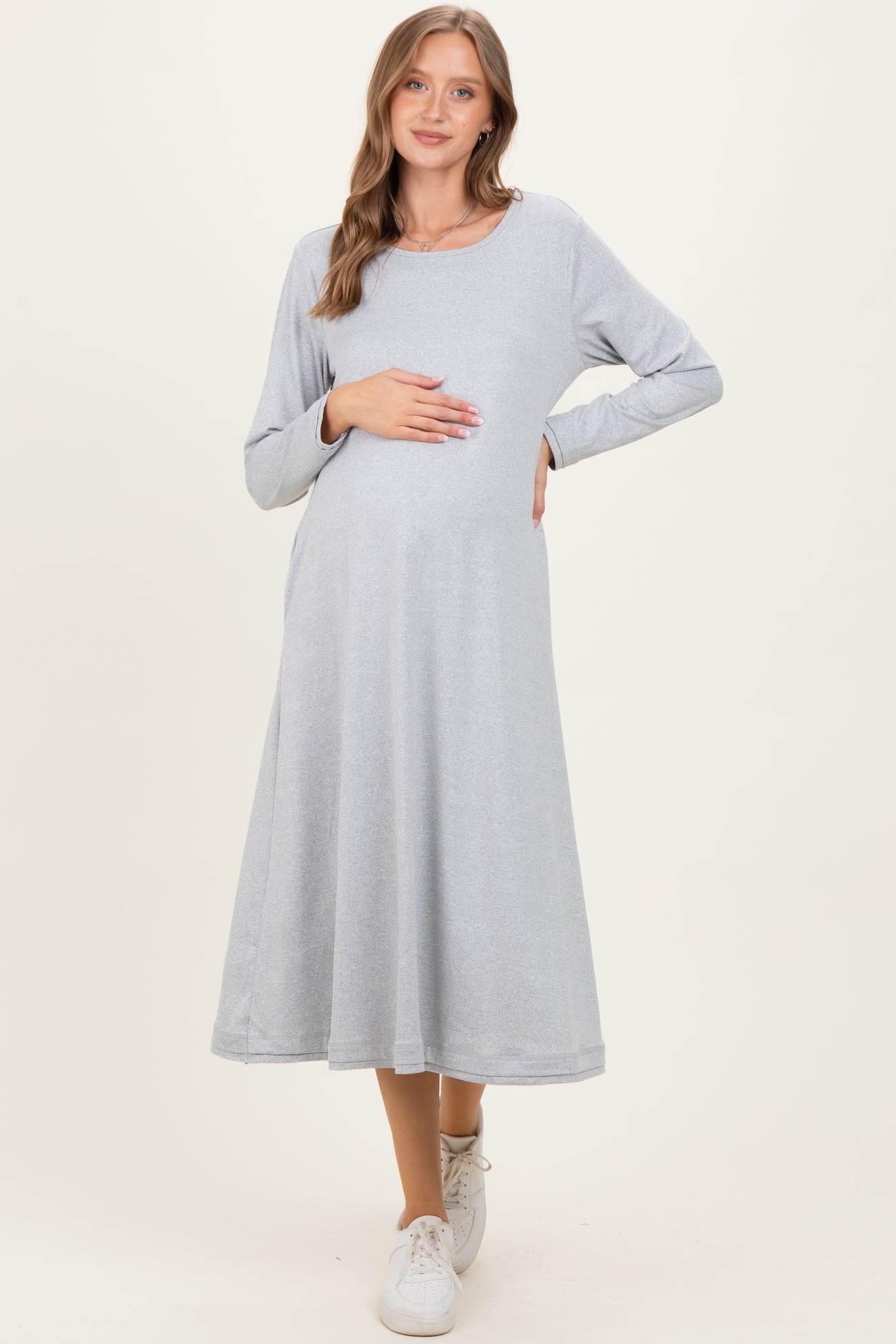 woman wearing a light grey long sleeve maternity dress and holding her baby bump